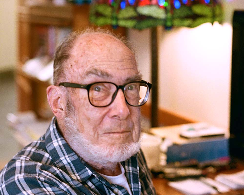 A senior man with glasses and facial hair sitting at a desk