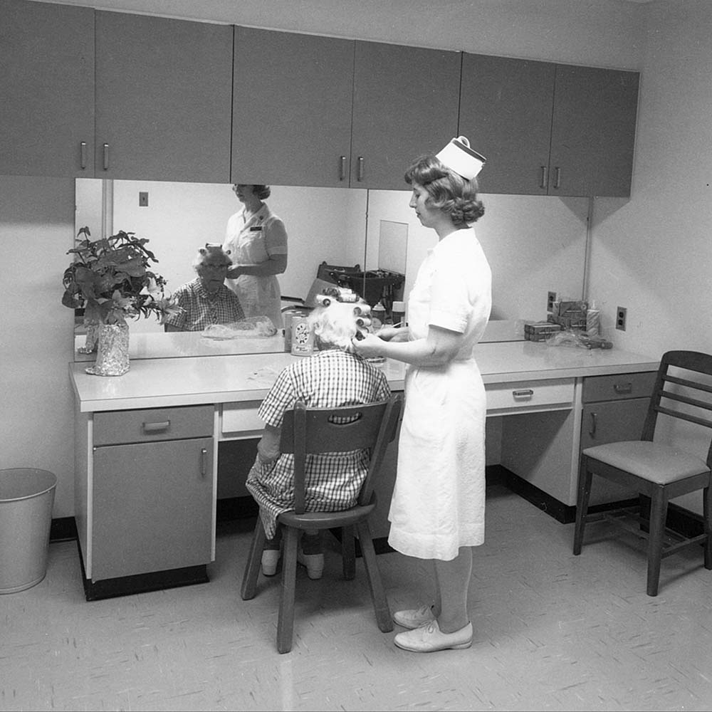 Black and white image of a nurse styling the hair of a senior
