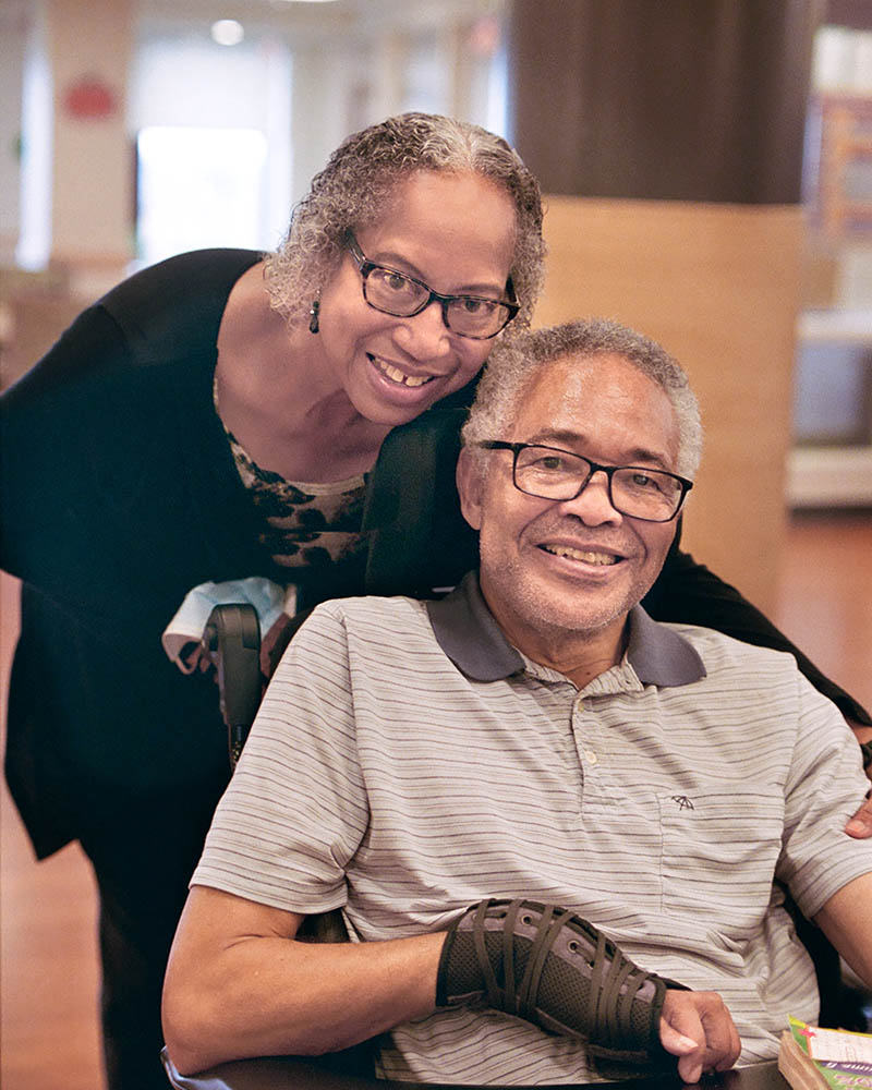 A smiling man in a wheelchair with a smiling woman behind him