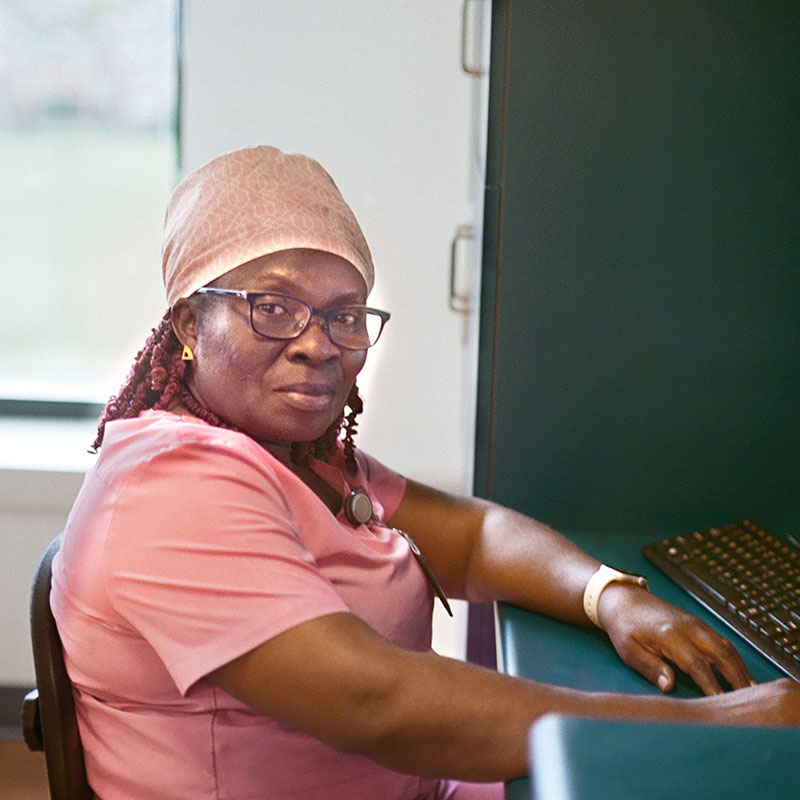 A care worker in pink scrubs sits behind a desk with a keyboard