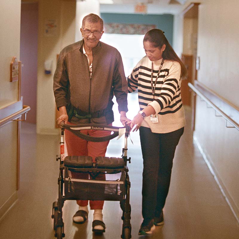 Woman helping senior man use walker in a hallway