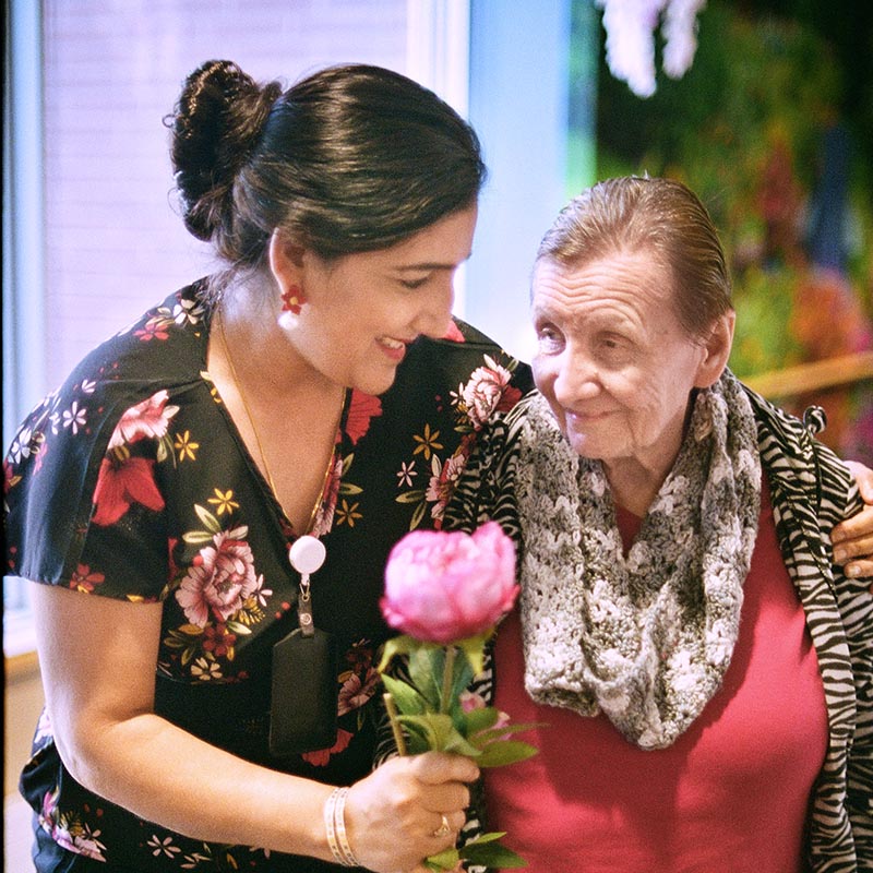Woman holding a flower for a senior woman, both smiling