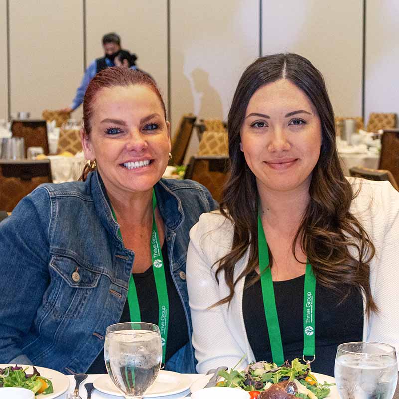 Two women at a dinner event table smiling at the camera