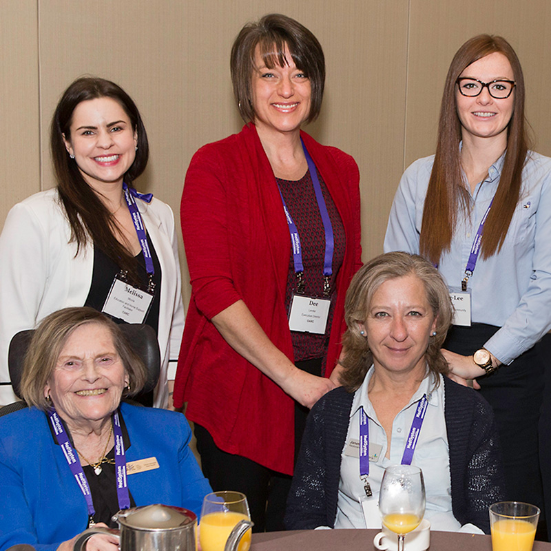 Group of 5 women smiling at the camera from behind a table